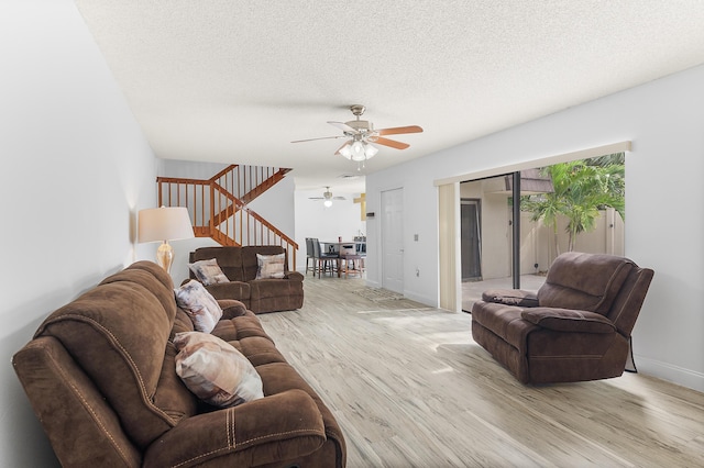 living room with stairway, a ceiling fan, baseboards, a textured ceiling, and light wood-type flooring