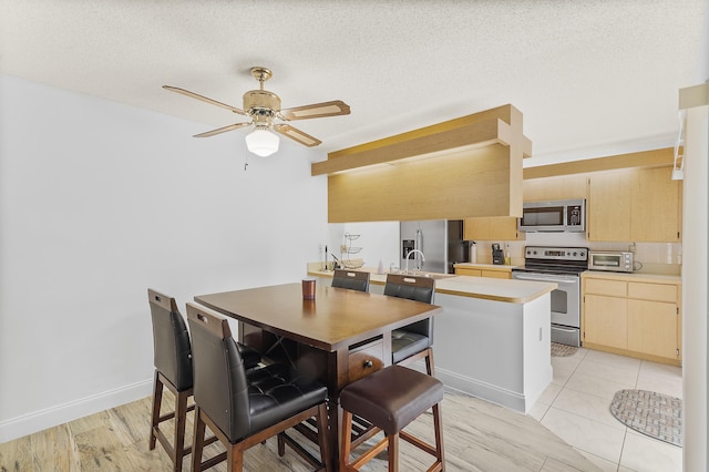 kitchen with a ceiling fan, a peninsula, light brown cabinetry, light countertops, and appliances with stainless steel finishes