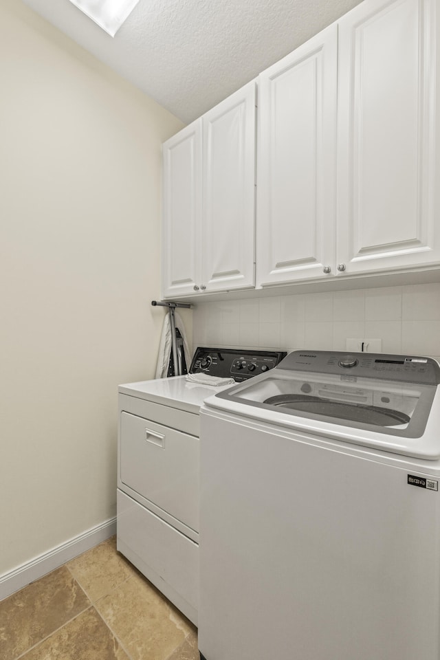 washroom with a textured ceiling, independent washer and dryer, cabinet space, and baseboards