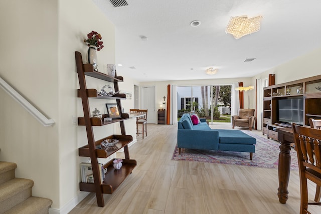 living area with baseboards, visible vents, light wood finished floors, and stairs