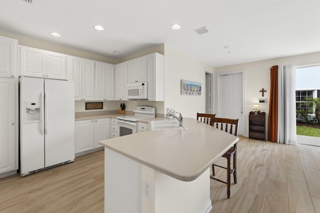 kitchen with white appliances, a kitchen breakfast bar, a peninsula, light countertops, and a sink