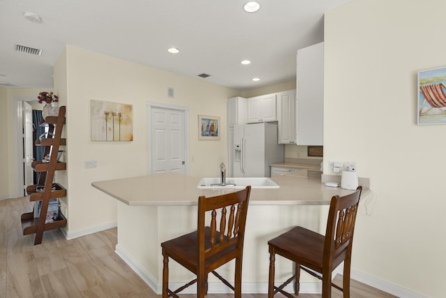 kitchen featuring a breakfast bar area, a peninsula, white refrigerator with ice dispenser, a sink, and visible vents