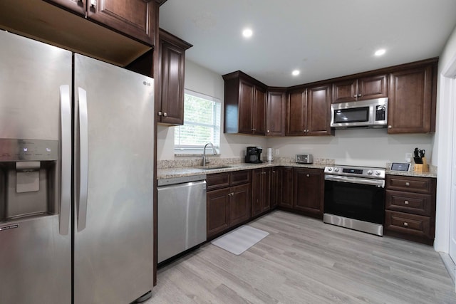 kitchen featuring light stone counters, appliances with stainless steel finishes, a sink, dark brown cabinetry, and light wood-type flooring