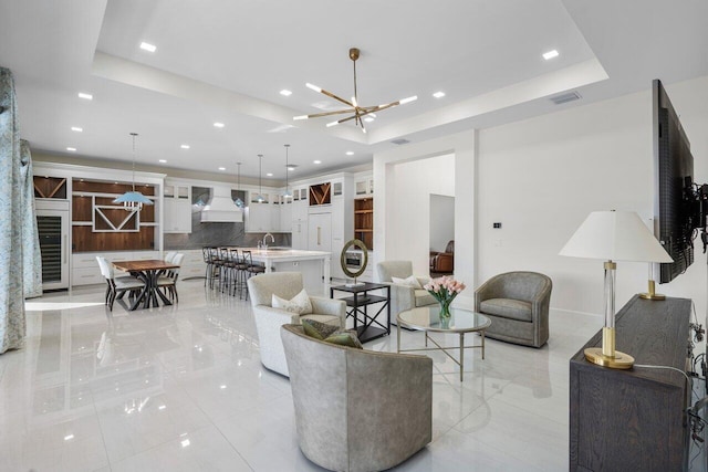 living room with a tray ceiling, a chandelier, and sink