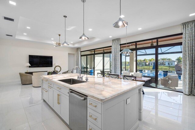 kitchen with dishwasher, white cabinetry, a tray ceiling, light stone countertops, and a center island with sink