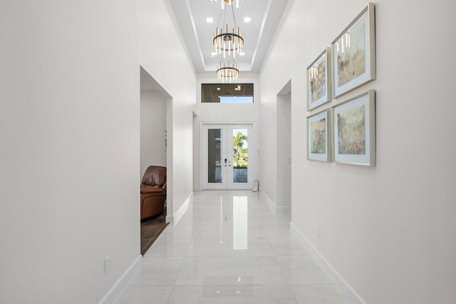 hallway with a towering ceiling, a tray ceiling, a chandelier, and french doors