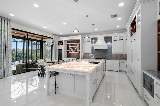 kitchen featuring white cabinetry, an island with sink, pendant lighting, and custom exhaust hood