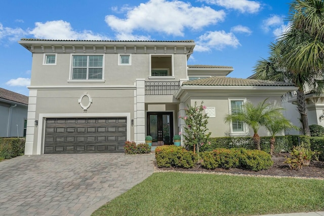 view of front of house featuring a tiled roof, an attached garage, decorative driveway, french doors, and stucco siding