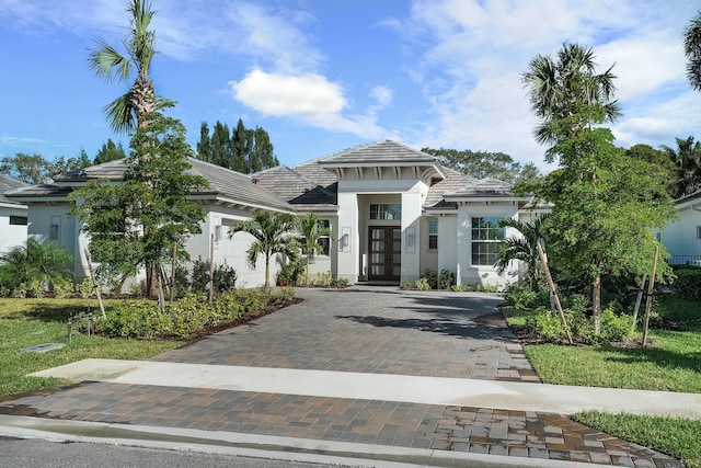 view of front of home with a garage, a tiled roof, decorative driveway, french doors, and stucco siding