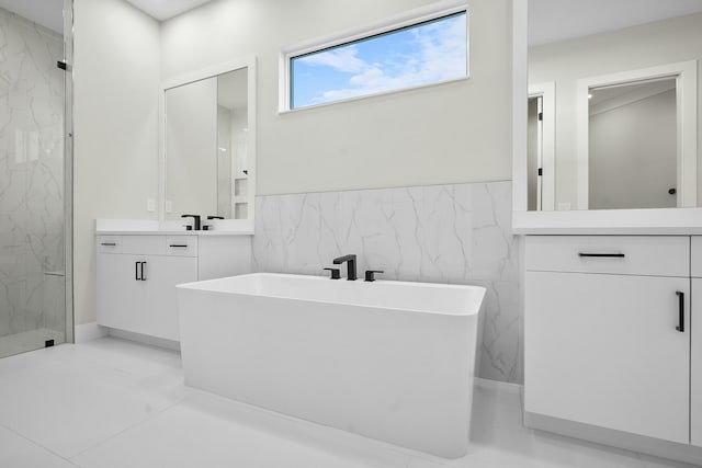 bathroom with tile walls, a freestanding bath, vanity, and a marble finish shower