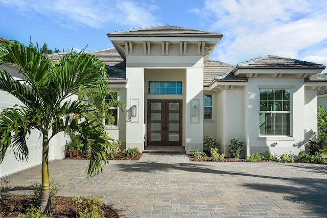 view of exterior entry featuring stucco siding, a tiled roof, and french doors