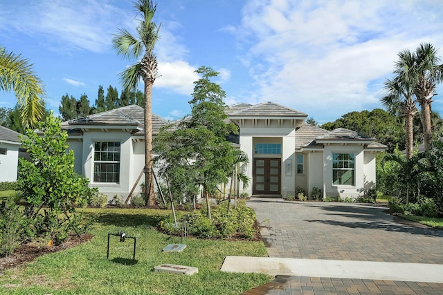 view of front facade featuring decorative driveway, french doors, a tile roof, stucco siding, and a front lawn