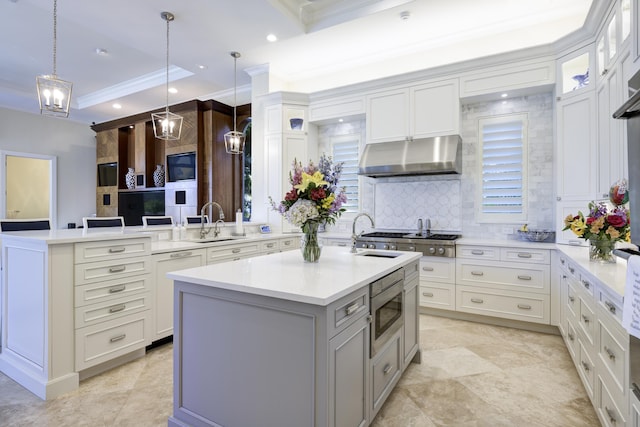 kitchen featuring appliances with stainless steel finishes, decorative light fixtures, sink, ornamental molding, and a center island with sink