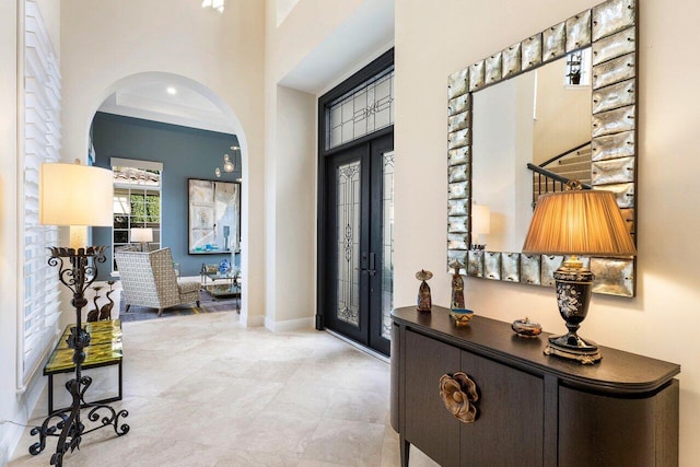 foyer entrance with crown molding, a towering ceiling, and french doors