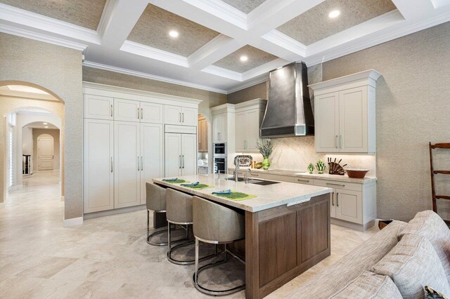 kitchen with crown molding, light stone countertops, white cabinets, and wall chimney exhaust hood