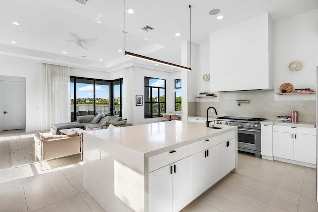 kitchen with white cabinetry, an island with sink, tasteful backsplash, and high end stove