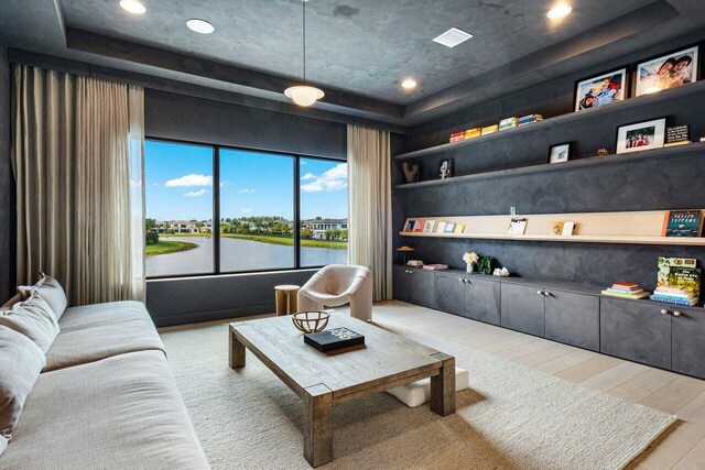 living room with a water view, a tray ceiling, light hardwood / wood-style floors, and built in shelves