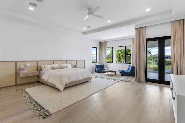 bedroom with ceiling fan, access to outside, light wood-type flooring, and a tray ceiling