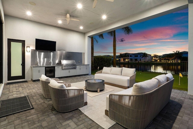 view of patio with an outdoor kitchen, an outdoor living space with a fire pit, beverage cooler, ceiling fan, and grilling area