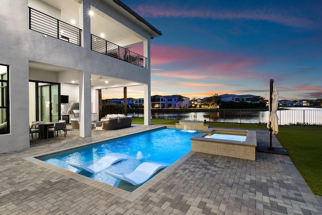 pool at dusk featuring a water view, an outdoor living space, a patio area, pool water feature, and an in ground hot tub