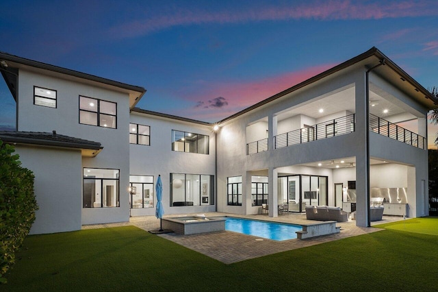 back house at dusk with a swimming pool with hot tub, a yard, an outdoor hangout area, and a balcony