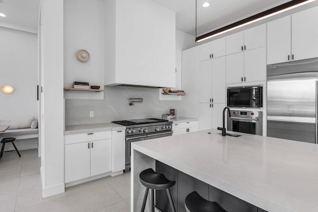 kitchen featuring built in appliances, light tile patterned floors, white cabinets, decorative backsplash, and wall chimney range hood