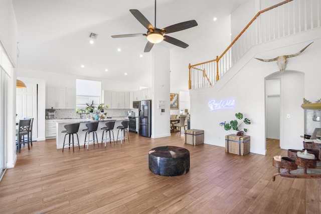 living room with ceiling fan, light hardwood / wood-style flooring, and a high ceiling