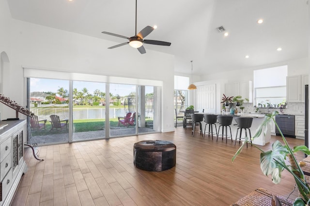 living room with a water view, ceiling fan, light hardwood / wood-style floors, and a towering ceiling