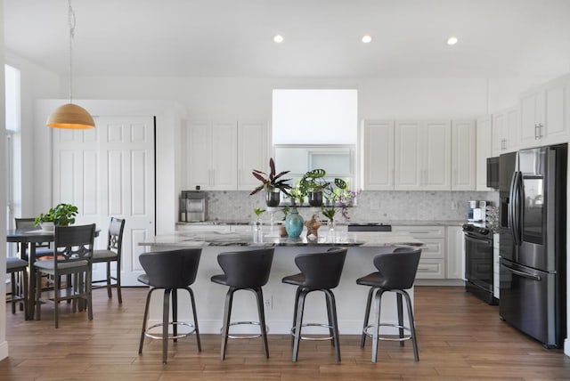 kitchen with stainless steel refrigerator with ice dispenser, white cabinetry, a kitchen bar, and light stone counters