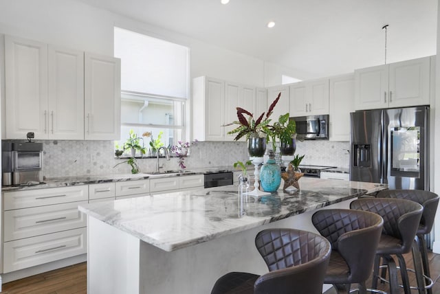 kitchen with sink, hanging light fixtures, stainless steel appliances, light stone countertops, and a kitchen island