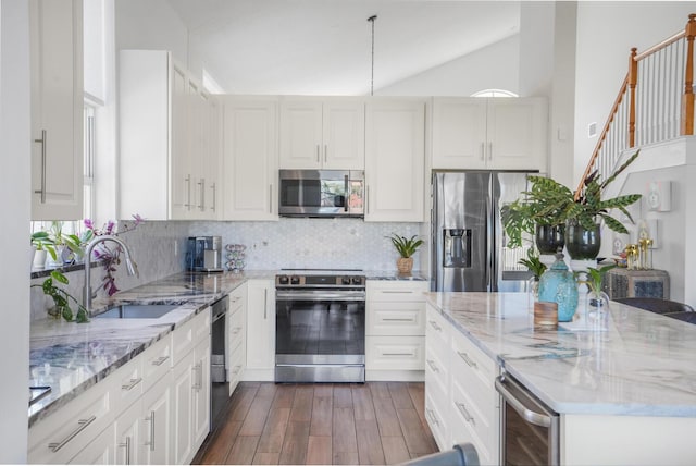 kitchen with vaulted ceiling, appliances with stainless steel finishes, sink, white cabinets, and light stone countertops