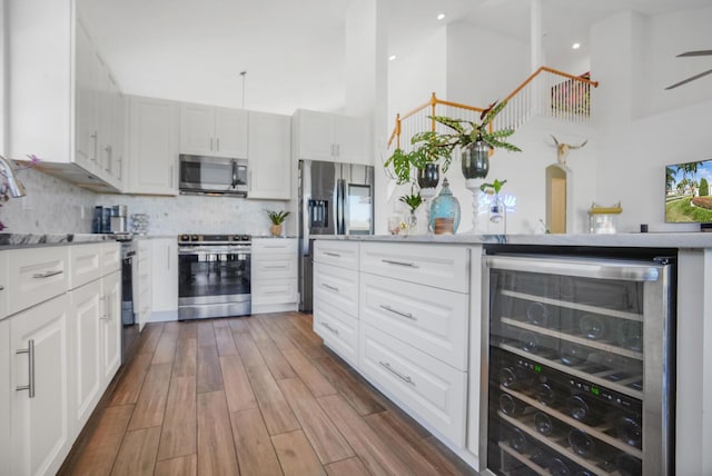 kitchen featuring appliances with stainless steel finishes, white cabinetry, dark hardwood / wood-style floors, wine cooler, and decorative backsplash