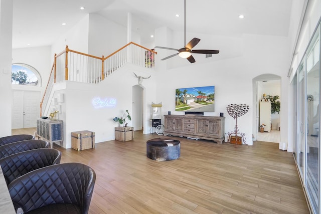 living room featuring a high ceiling, ceiling fan, and light wood-type flooring