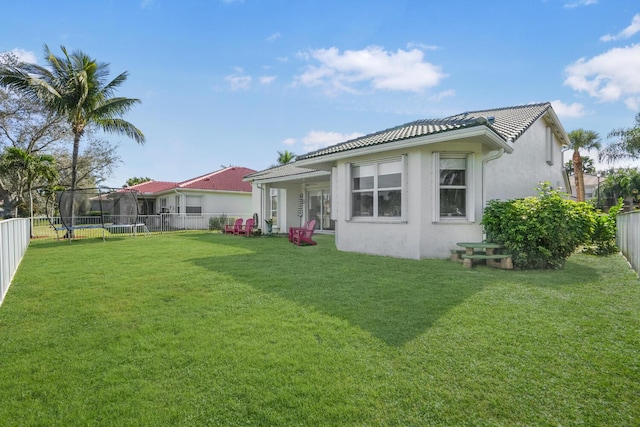 rear view of house featuring a trampoline and a lawn