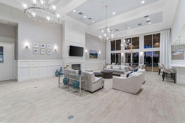 living room featuring a towering ceiling, a fireplace, light hardwood / wood-style flooring, and a notable chandelier