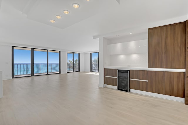 interior space featuring wine cooler, expansive windows, light hardwood / wood-style floors, a water view, and bar area