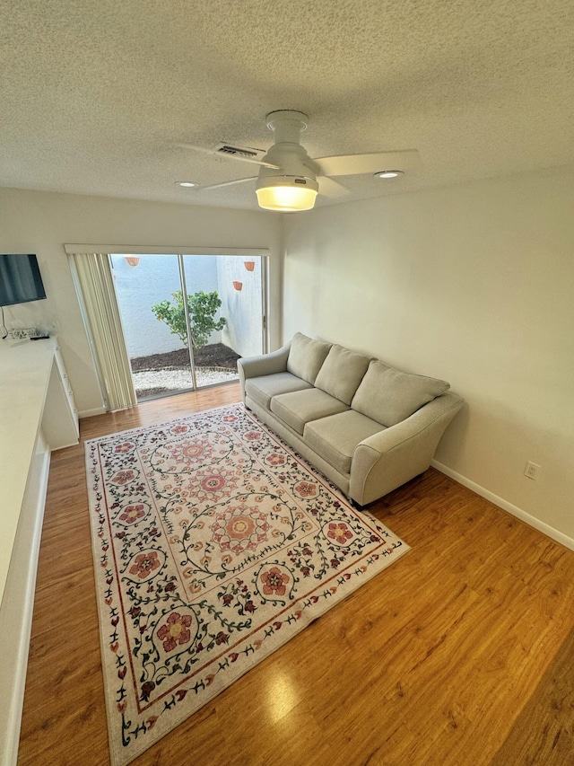 living room with hardwood / wood-style flooring, a textured ceiling, and ceiling fan