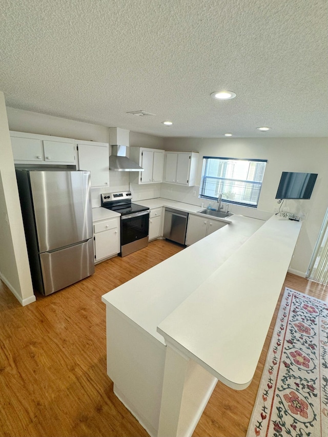 kitchen with white cabinetry, appliances with stainless steel finishes, kitchen peninsula, and wall chimney range hood