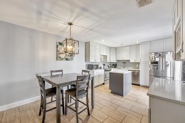 kitchen with sink, stainless steel appliances, light stone counters, a kitchen island, and decorative light fixtures