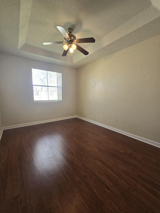 unfurnished room featuring dark wood-type flooring, ceiling fan, a raised ceiling, and a textured ceiling