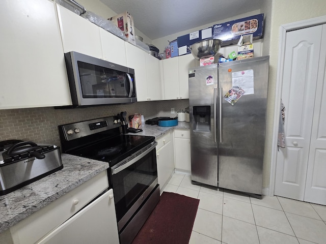 kitchen featuring tasteful backsplash, light tile patterned floors, stainless steel appliances, light stone countertops, and white cabinets