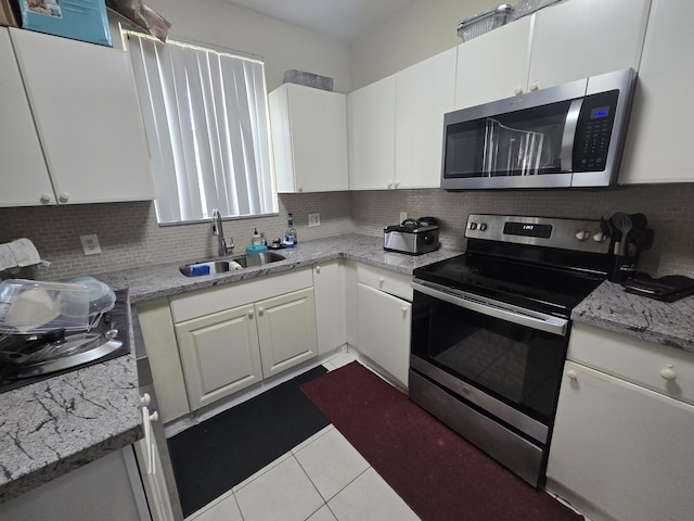 kitchen featuring sink, white cabinetry, stainless steel appliances, light tile patterned flooring, and decorative backsplash