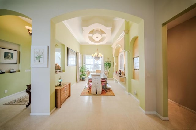 hallway with light tile patterned floors, ornamental molding, a raised ceiling, and a chandelier