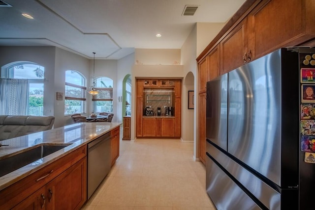 kitchen with light tile patterned flooring, sink, light stone counters, pendant lighting, and stainless steel appliances