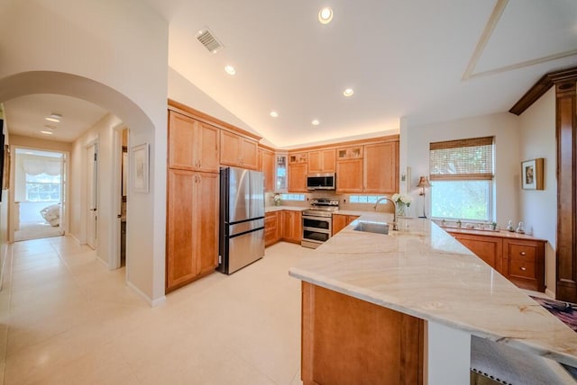 kitchen with sink, plenty of natural light, kitchen peninsula, stainless steel appliances, and light stone countertops