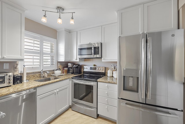 kitchen with sink, white cabinetry, hanging light fixtures, stainless steel appliances, and light stone countertops