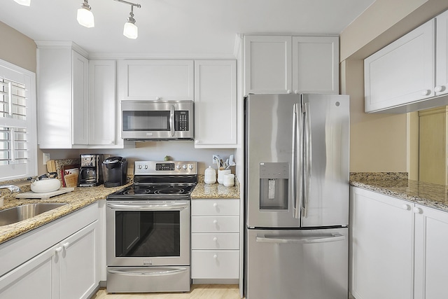 kitchen featuring appliances with stainless steel finishes, sink, white cabinets, hanging light fixtures, and light stone countertops