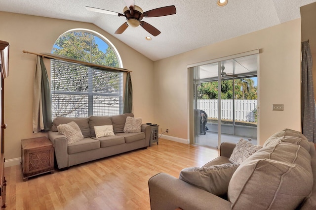 living room with ceiling fan, plenty of natural light, vaulted ceiling, and light wood-type flooring