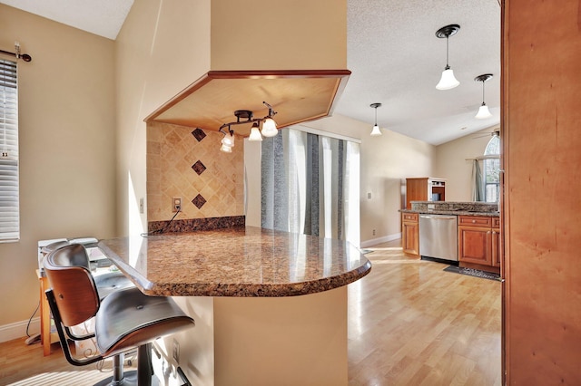 kitchen with decorative light fixtures, dishwasher, lofted ceiling, a breakfast bar area, and kitchen peninsula