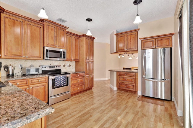 kitchen featuring stainless steel appliances, tasteful backsplash, light hardwood / wood-style floors, and decorative light fixtures